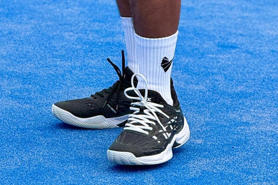Padel player wearing white grip socks and black padel shoes on a blue court
