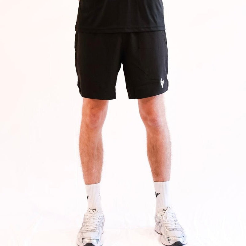 Male athlete wearing black athletic Padel Source Pro Performance 7" shorts on a white background