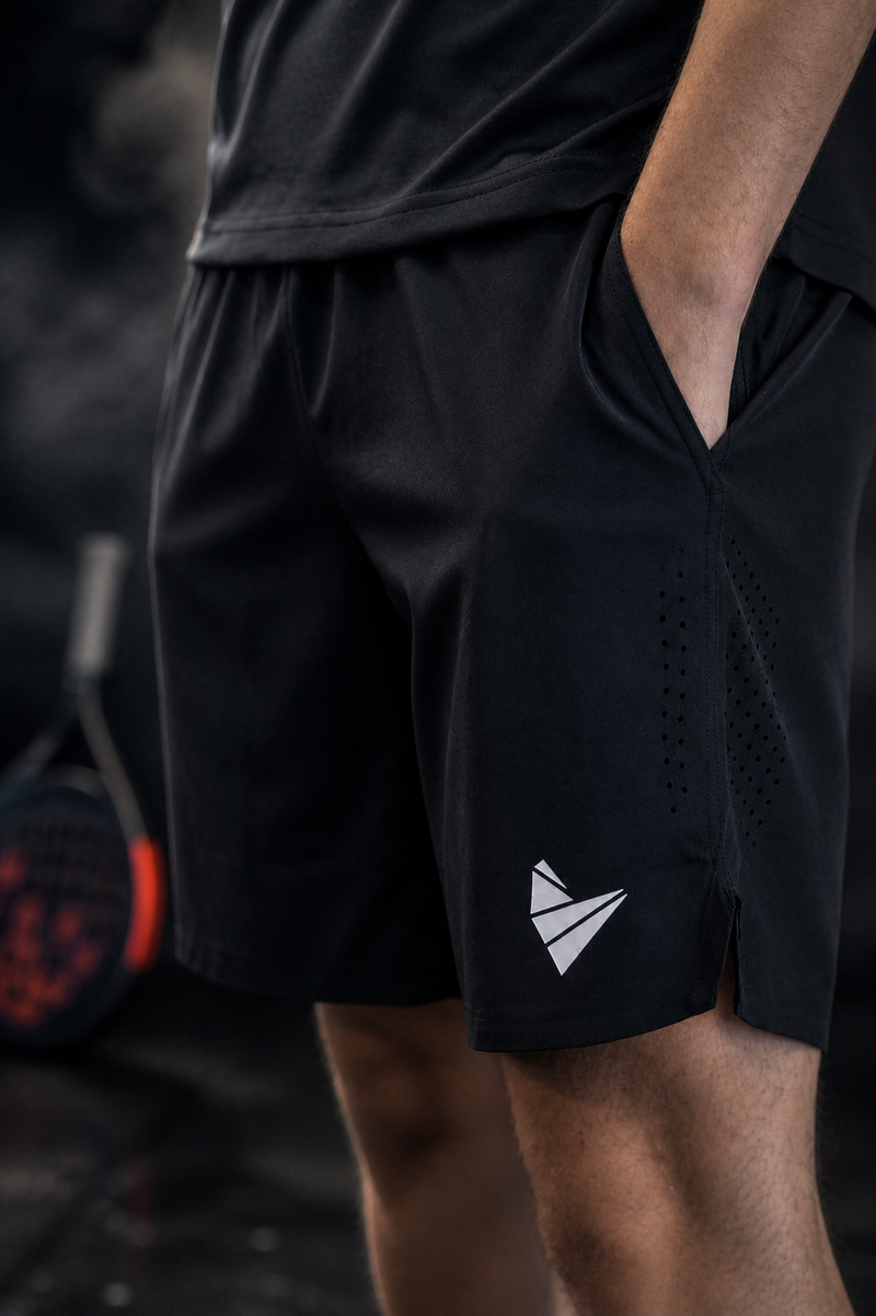 Comfortable, well-fitted padel clothing shorts displayed on a black smokey background on a model, and a padel racket in the background.