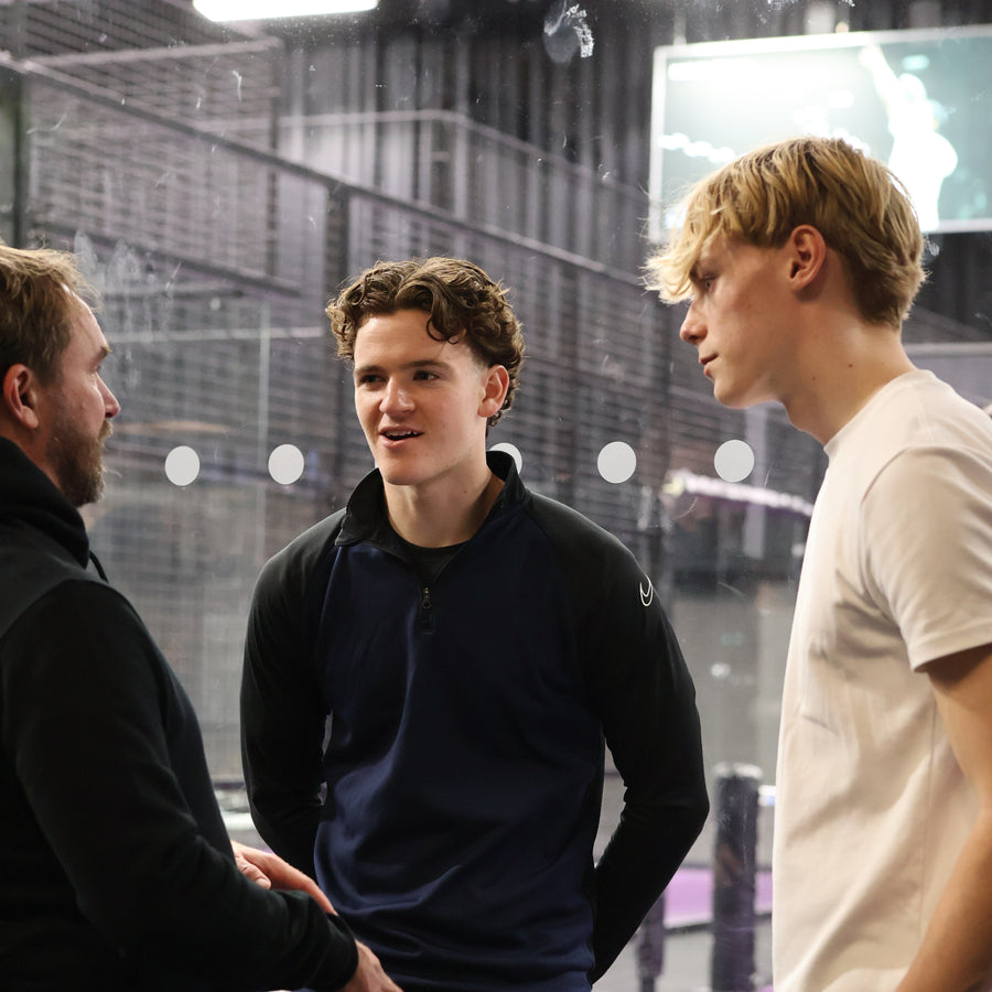 Three men are engaged in a conversation on a sports court.